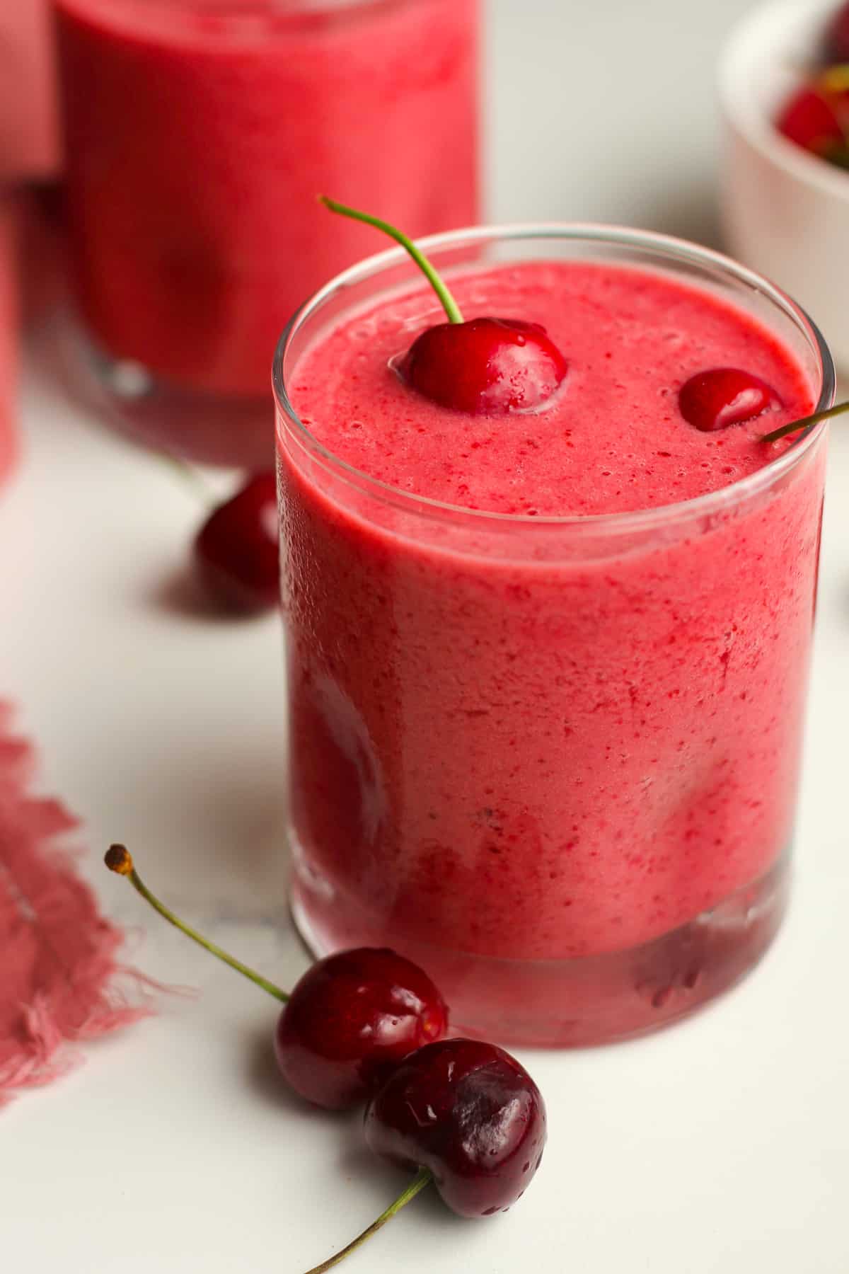 Side shot of a cherry smoothie with fresh cherries on top.
