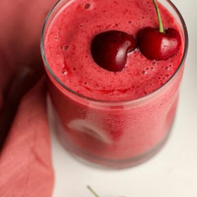 Side shot of a glass of cherry smoothie with fresh cherries.