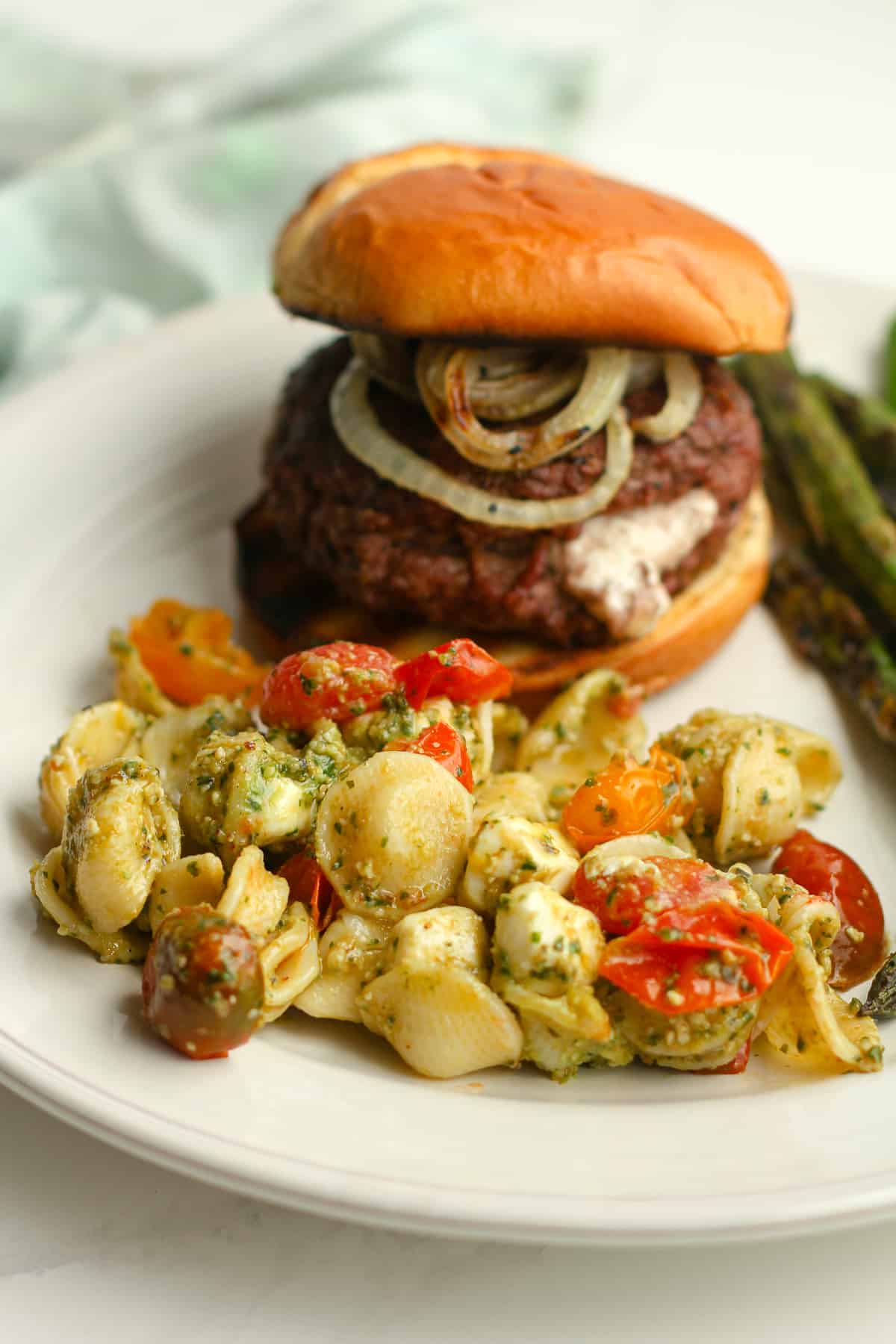 Side shot of a plate of pasta salad with a burger.