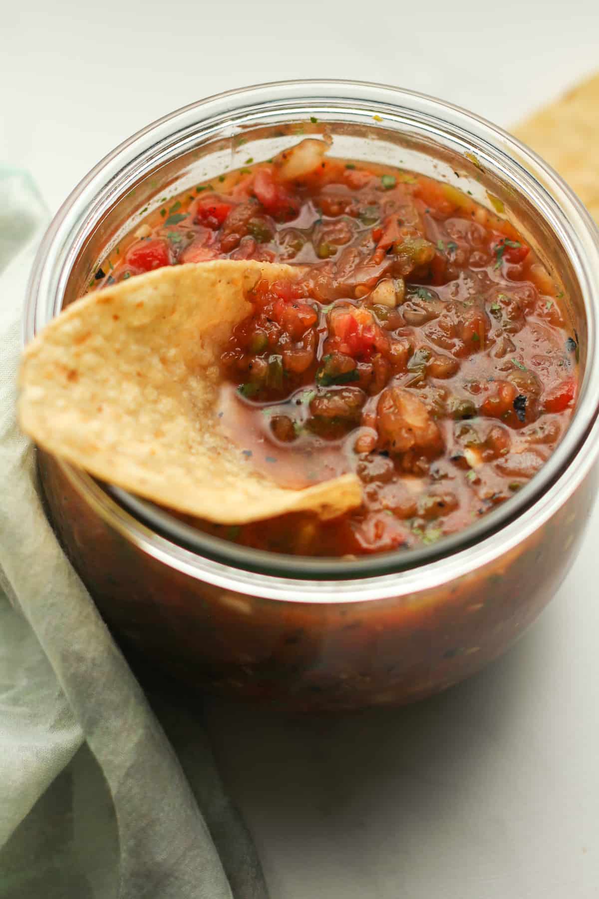 A closeup on a jar of grilled salsa with a chip.