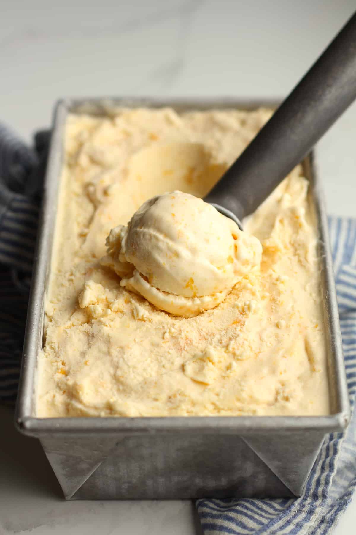 Side shot of a pan of peach ice cream with an ice cream scoop.