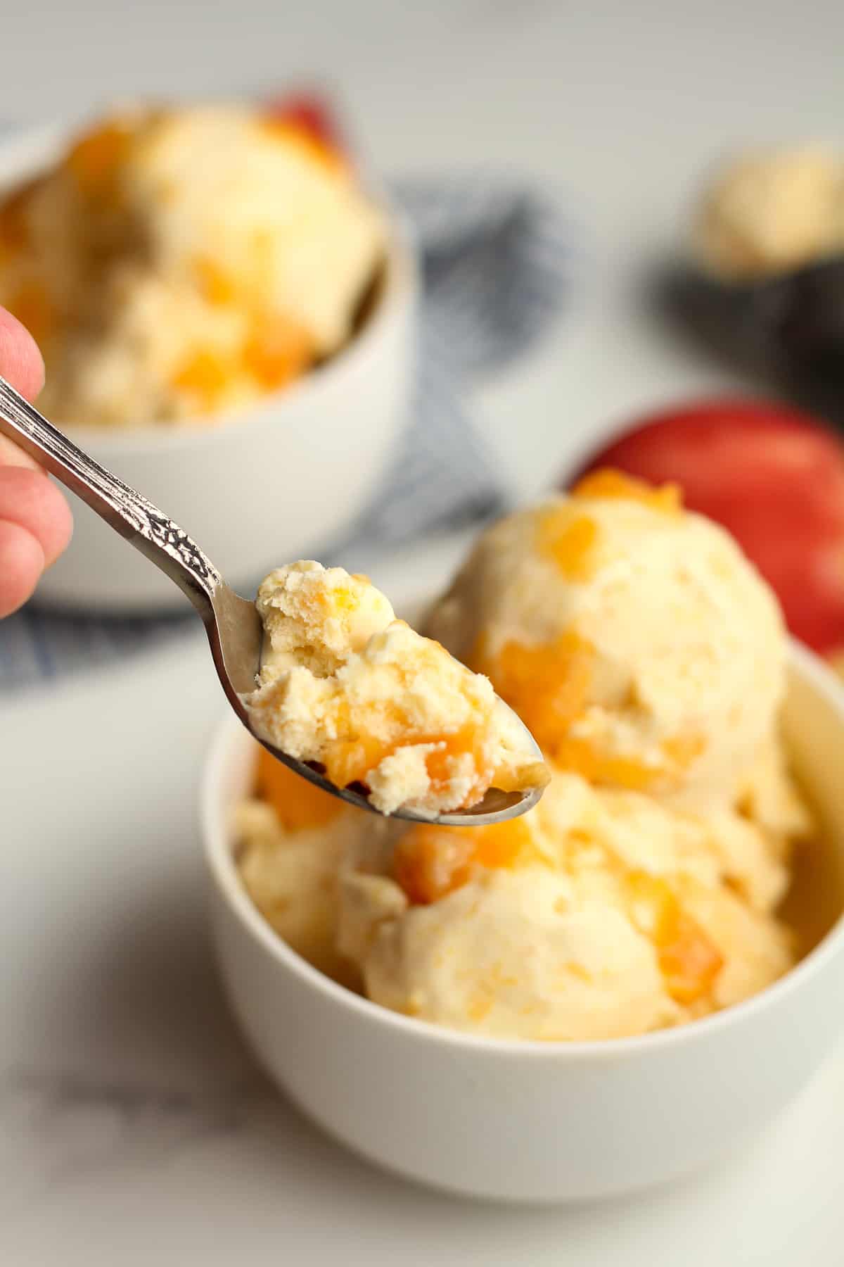 A spoonful of homemade peach ice cream, by a bowl.