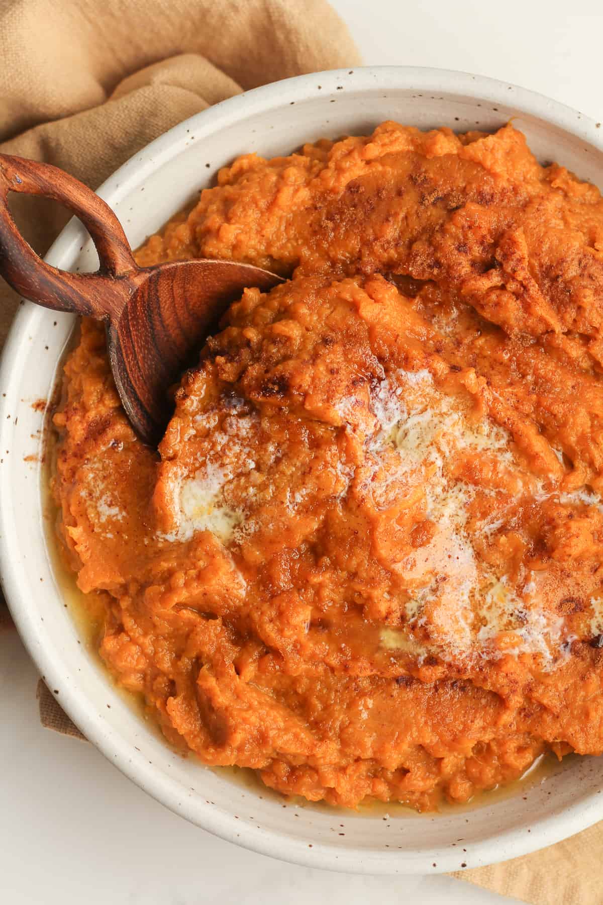 Closeup shot of a bowl of mashed sweet potatoes with a wooden spoon.