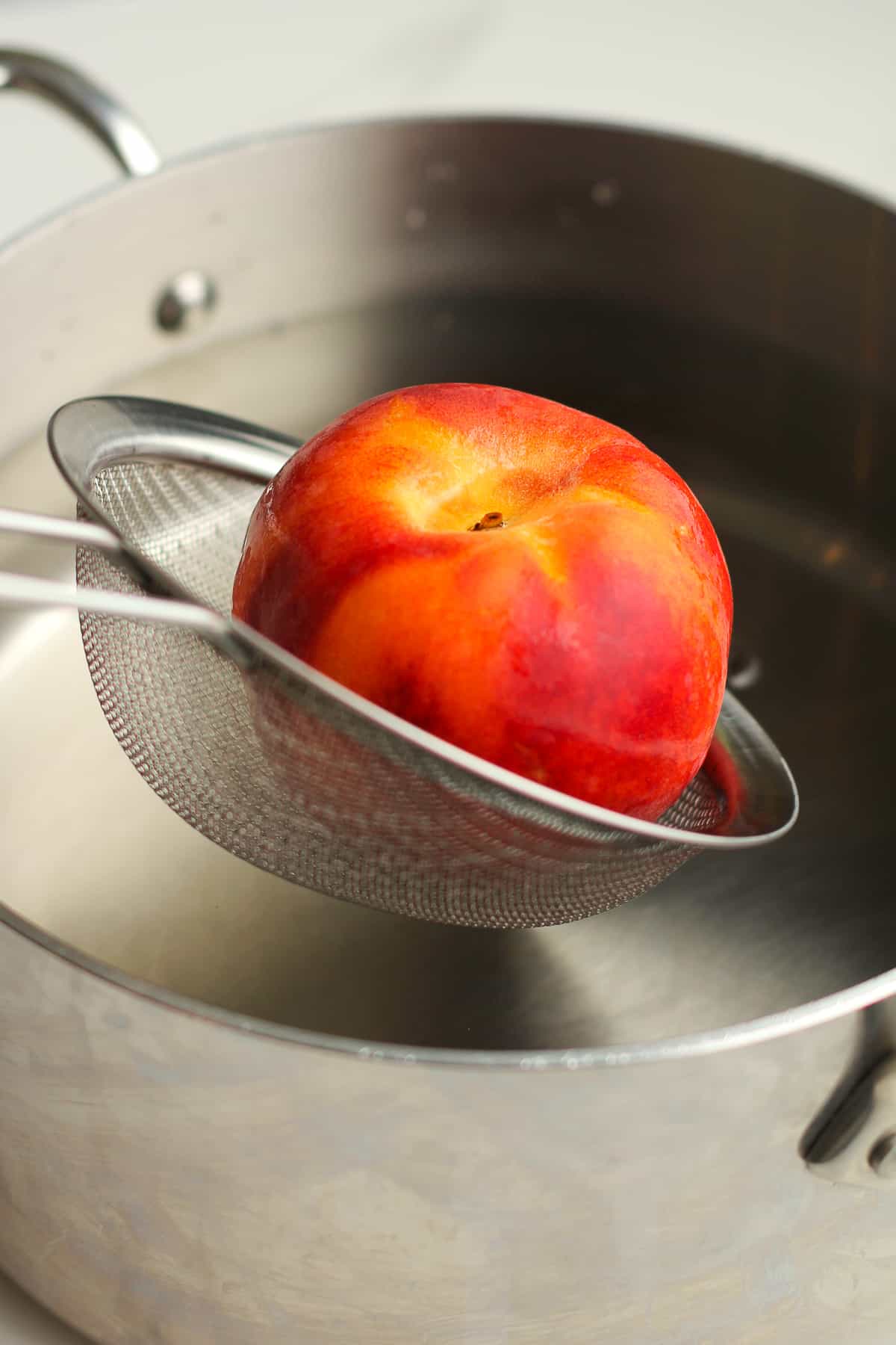 A pan of boiling water with a strainer pulling out a peach.