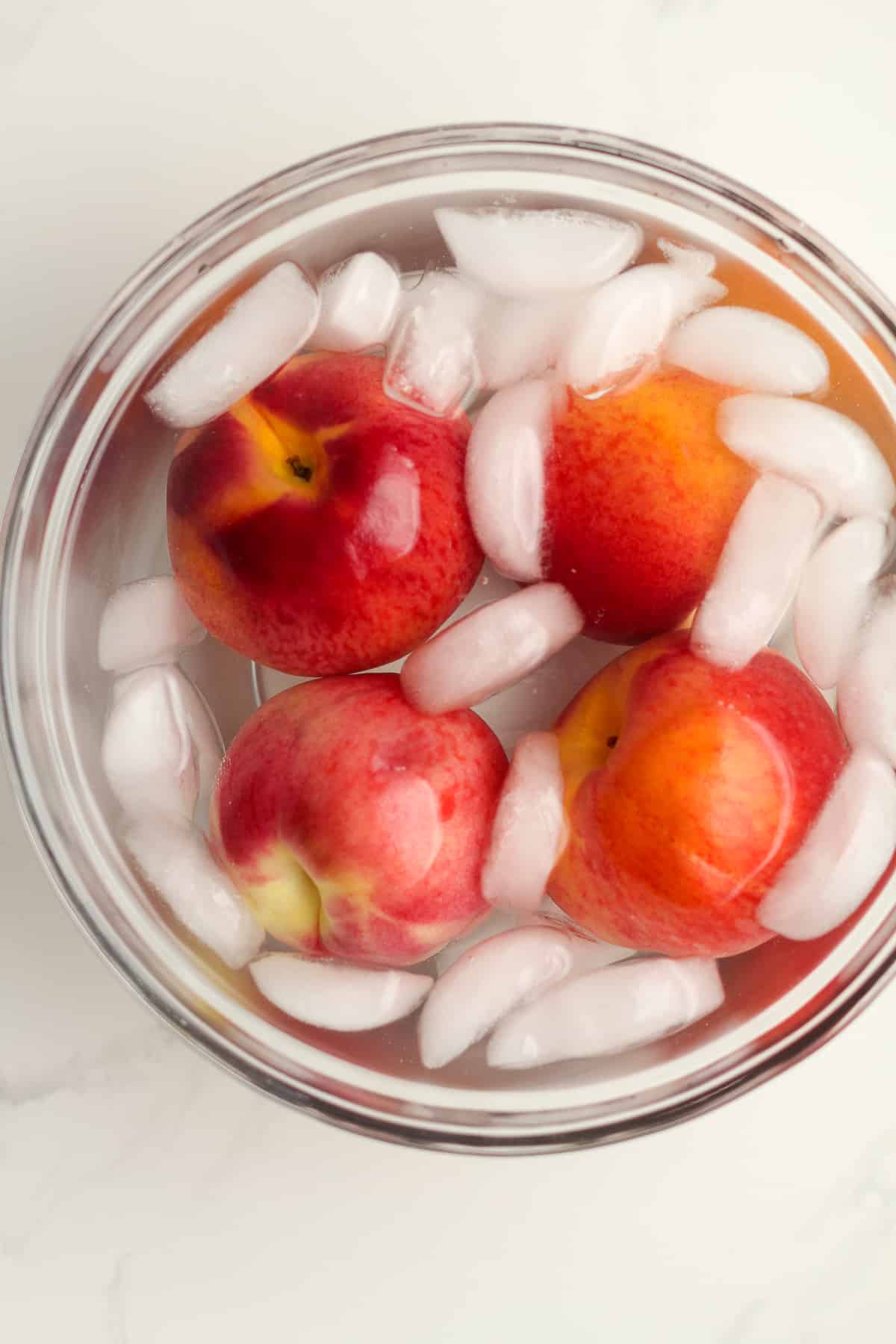 A glass bowl of peaches in an ice bath.
