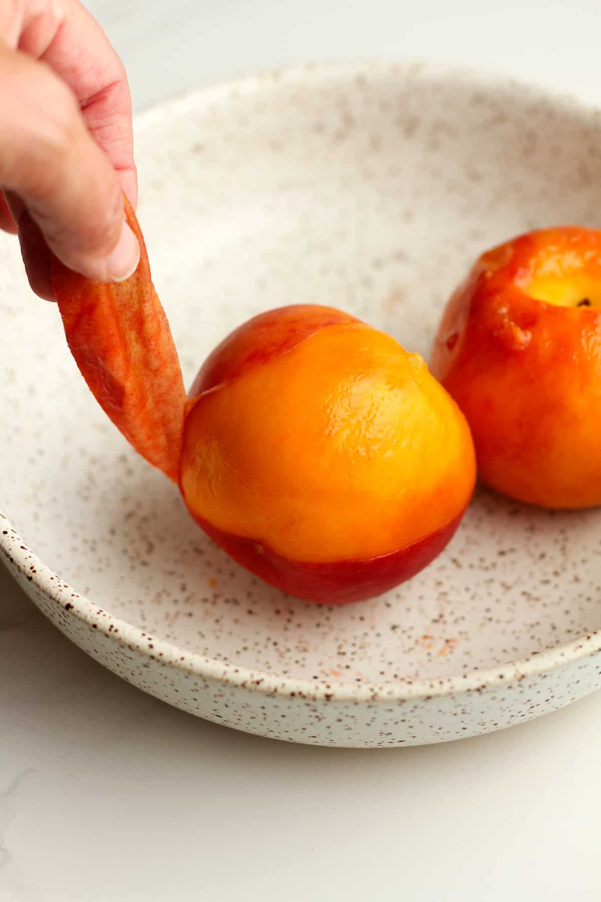 A hand pulling the skin off of a peach.