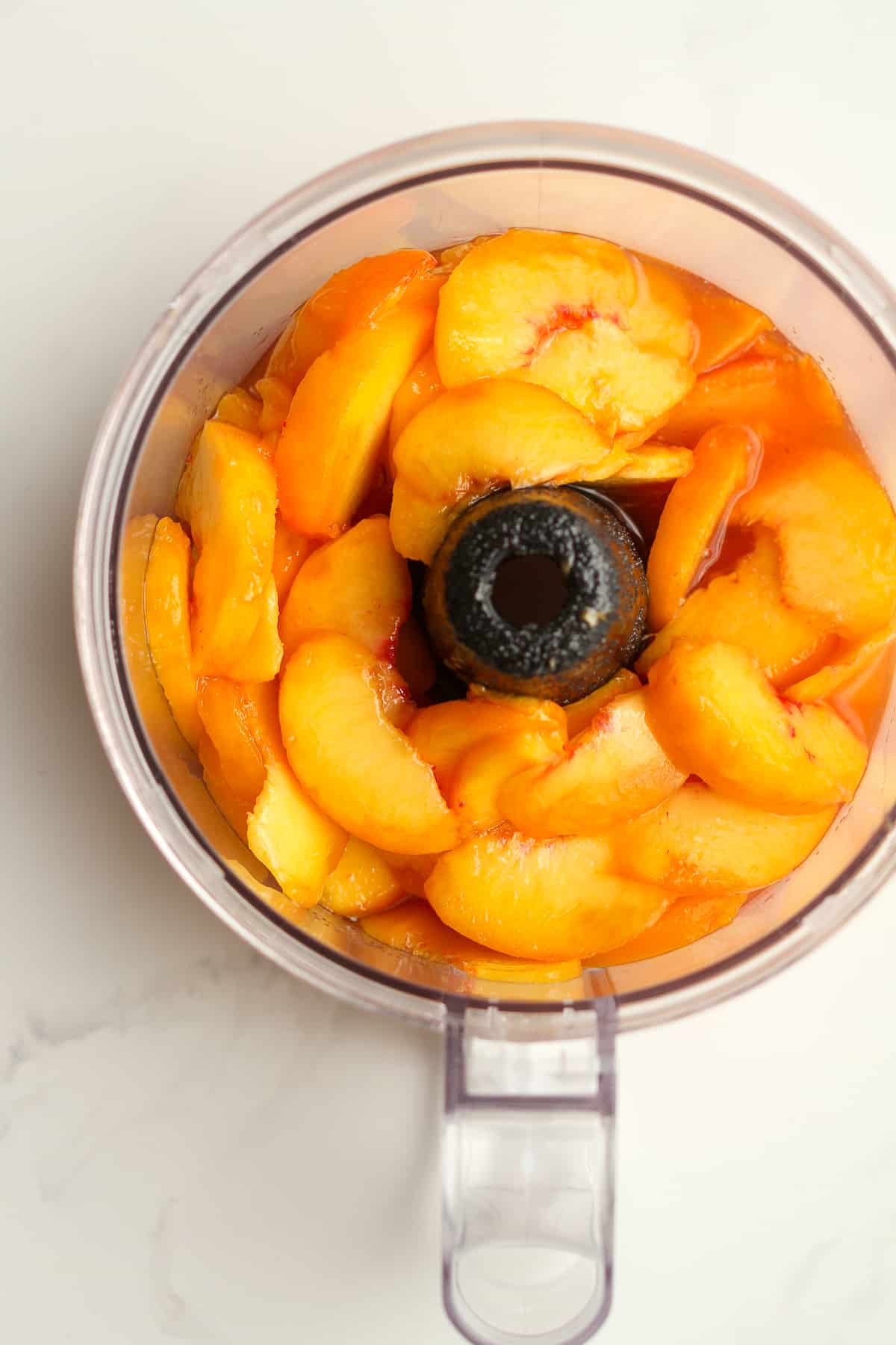 A food processor of sliced peaches and sugar.