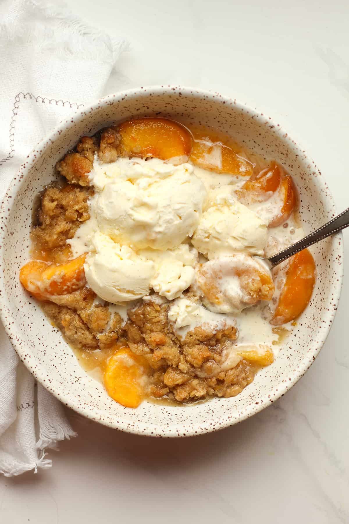 A bowl of peach cobbler with vanilla bean ice cream.