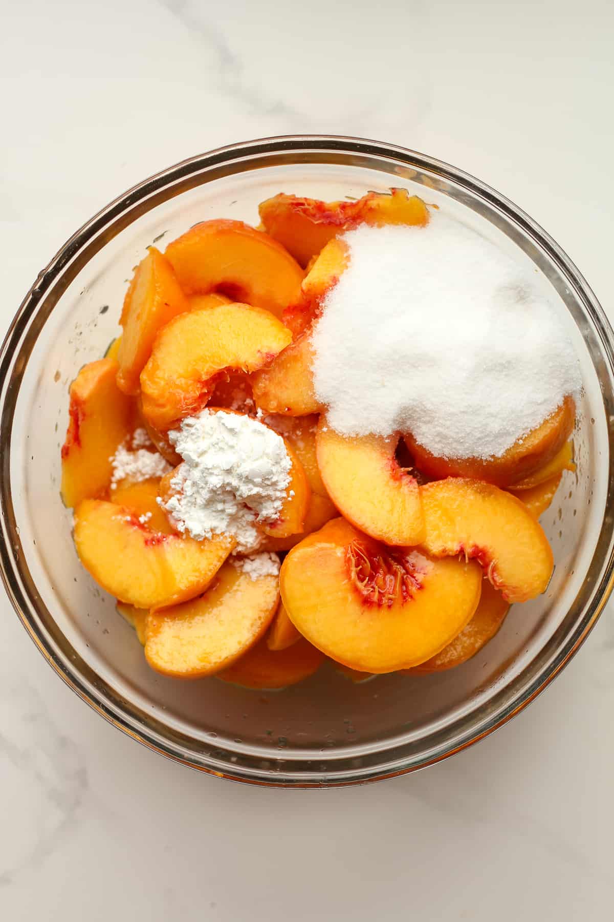 A bowl of sliced peaches plus sugar and other ingredients.