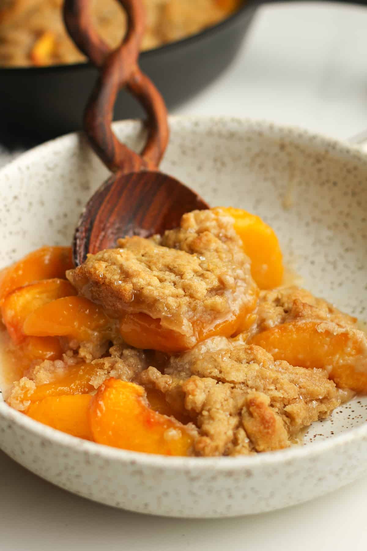 A wooden spoon serving a bowl of peach cobbler.