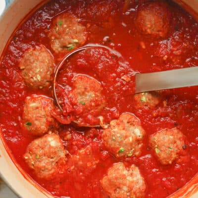 A stock pot of meatballs and sauce with a ladle.
