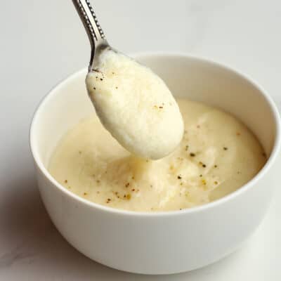 A spoon of the white sauce over a bowl.