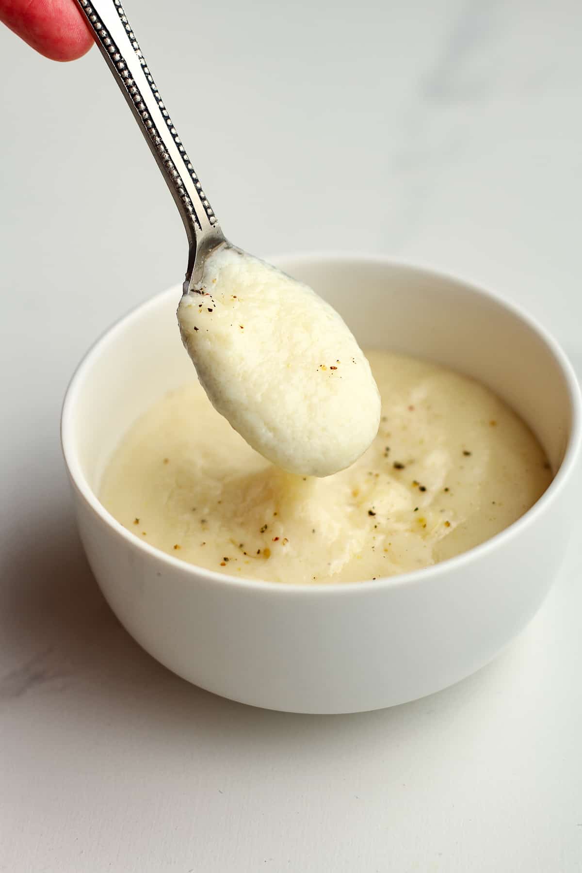 A spoon of the white sauce over a bowl.