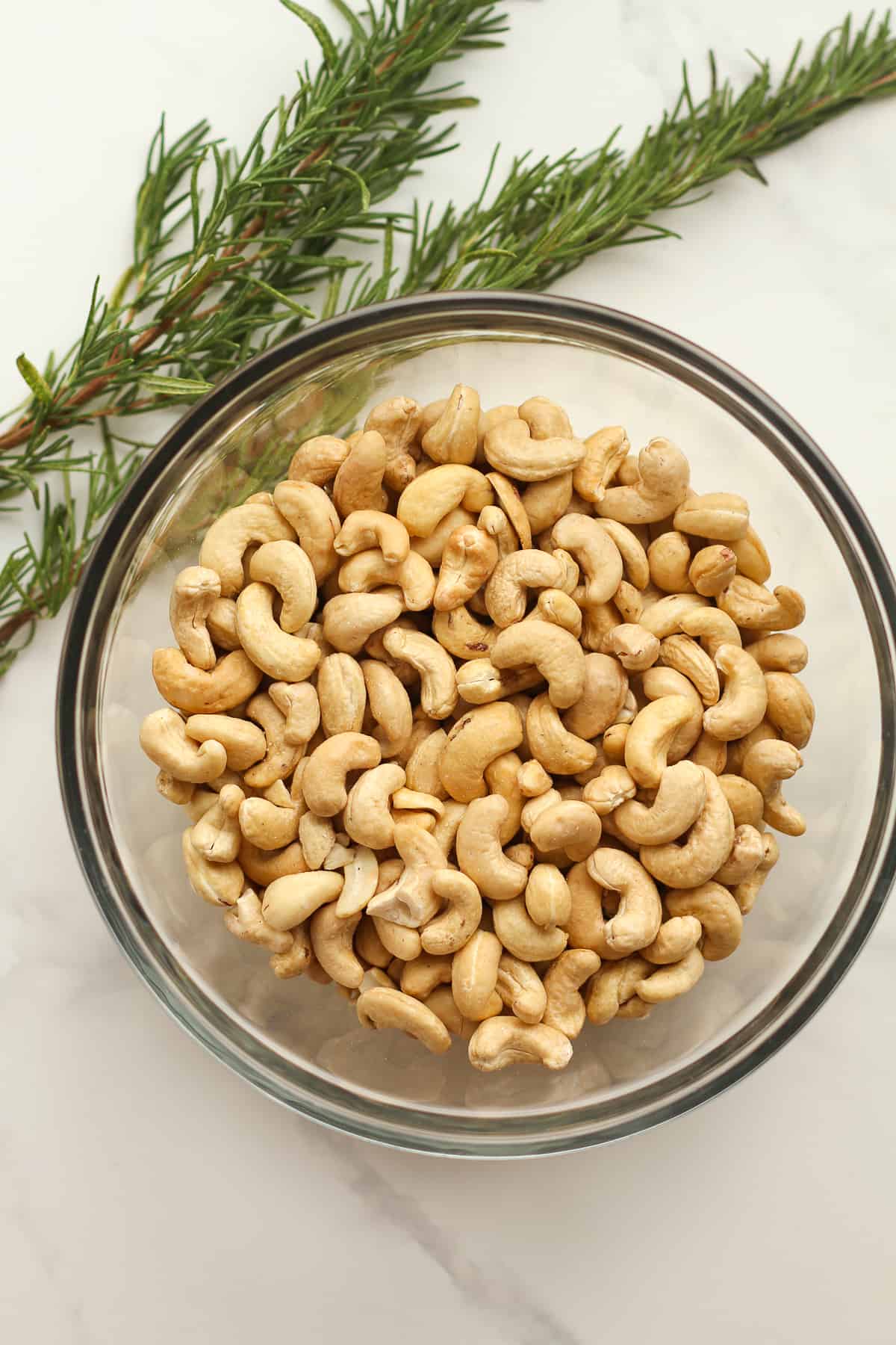 A bowl of raw cashews with some rosemary sprigs.