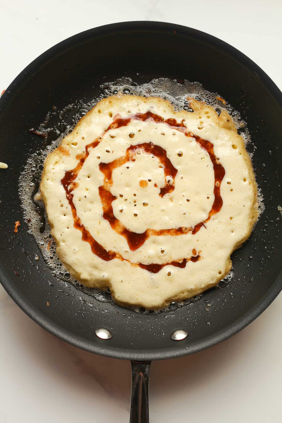 A pancake cooking in a pan with a swirl.