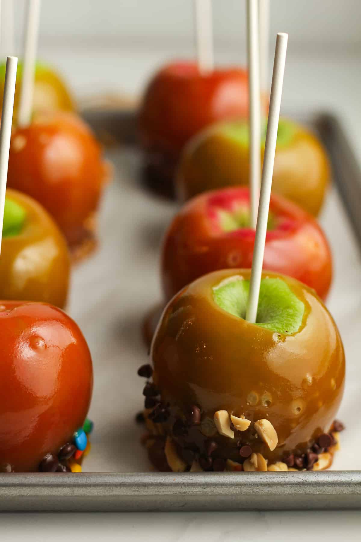 Side shot of a tray of caramel apples with toppings.