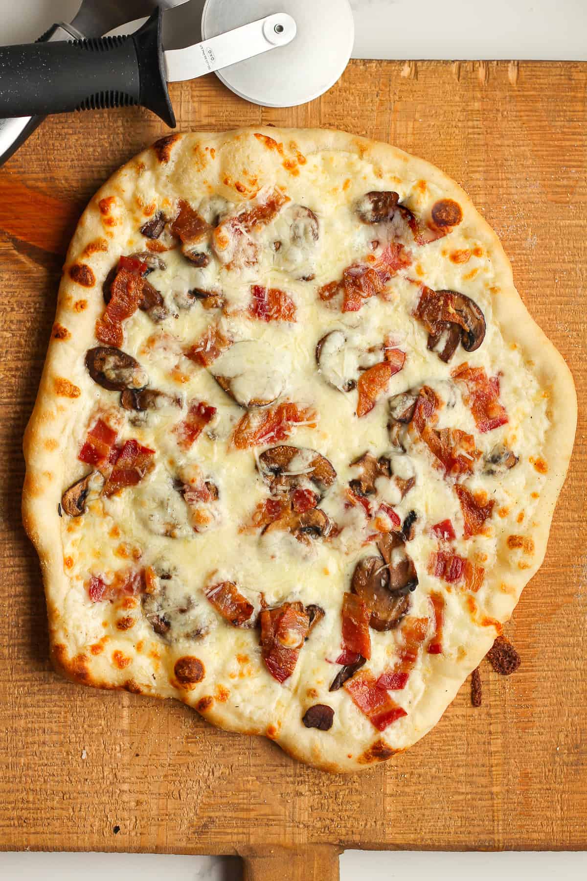 A grilled white sauce pizza on a wooden board.