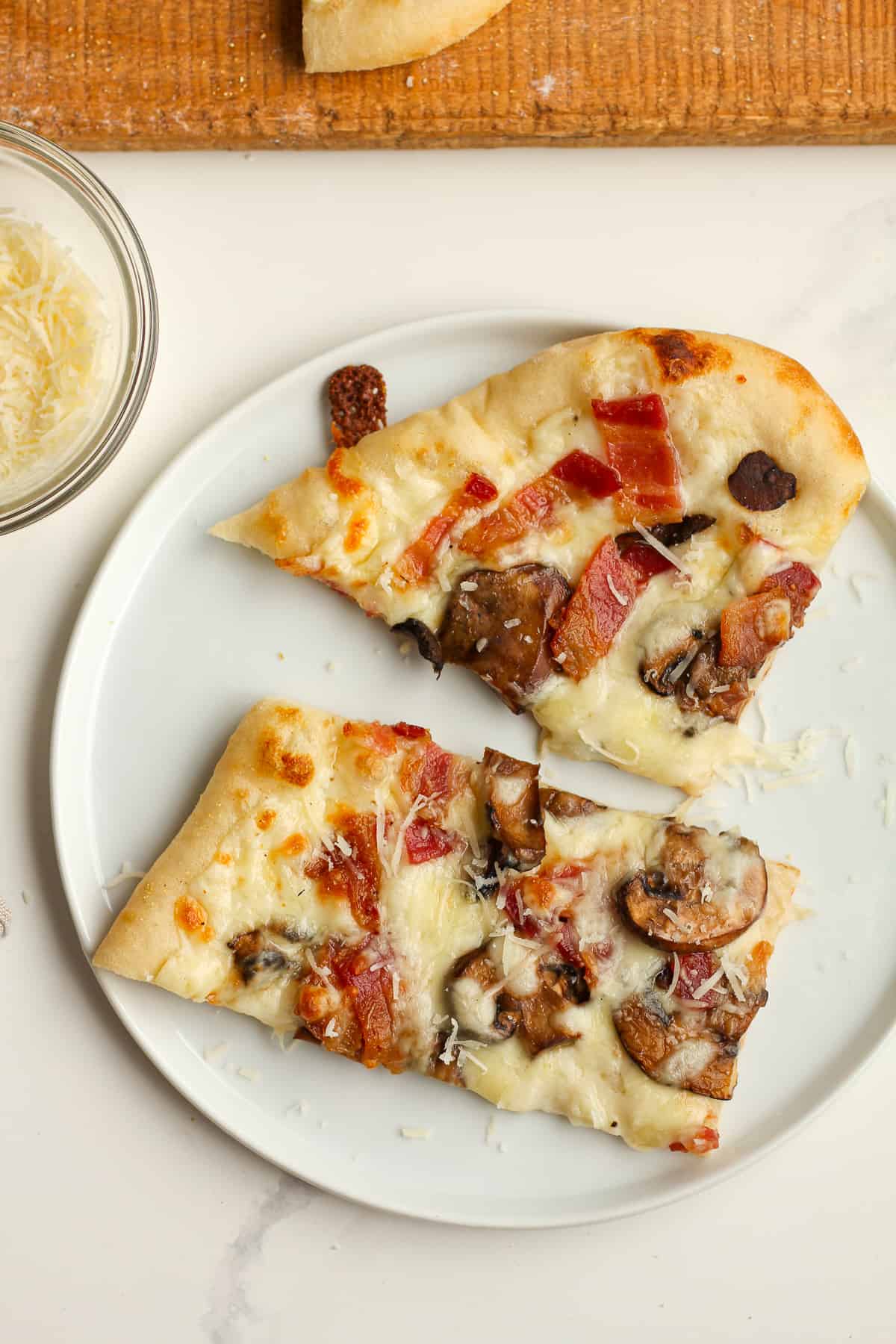 Two slices of white sauce pizza with bacon and mushrooms.