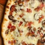 A just grilled white sauce pizza with bacon and mushrooms.