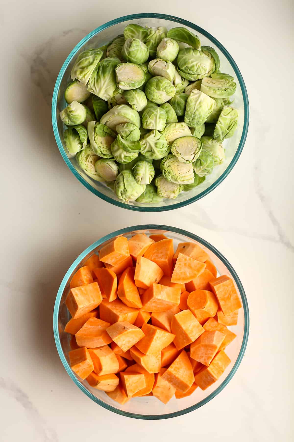 A bowl of chopped Brussels sprouts and another of chopped sweet potatoes.