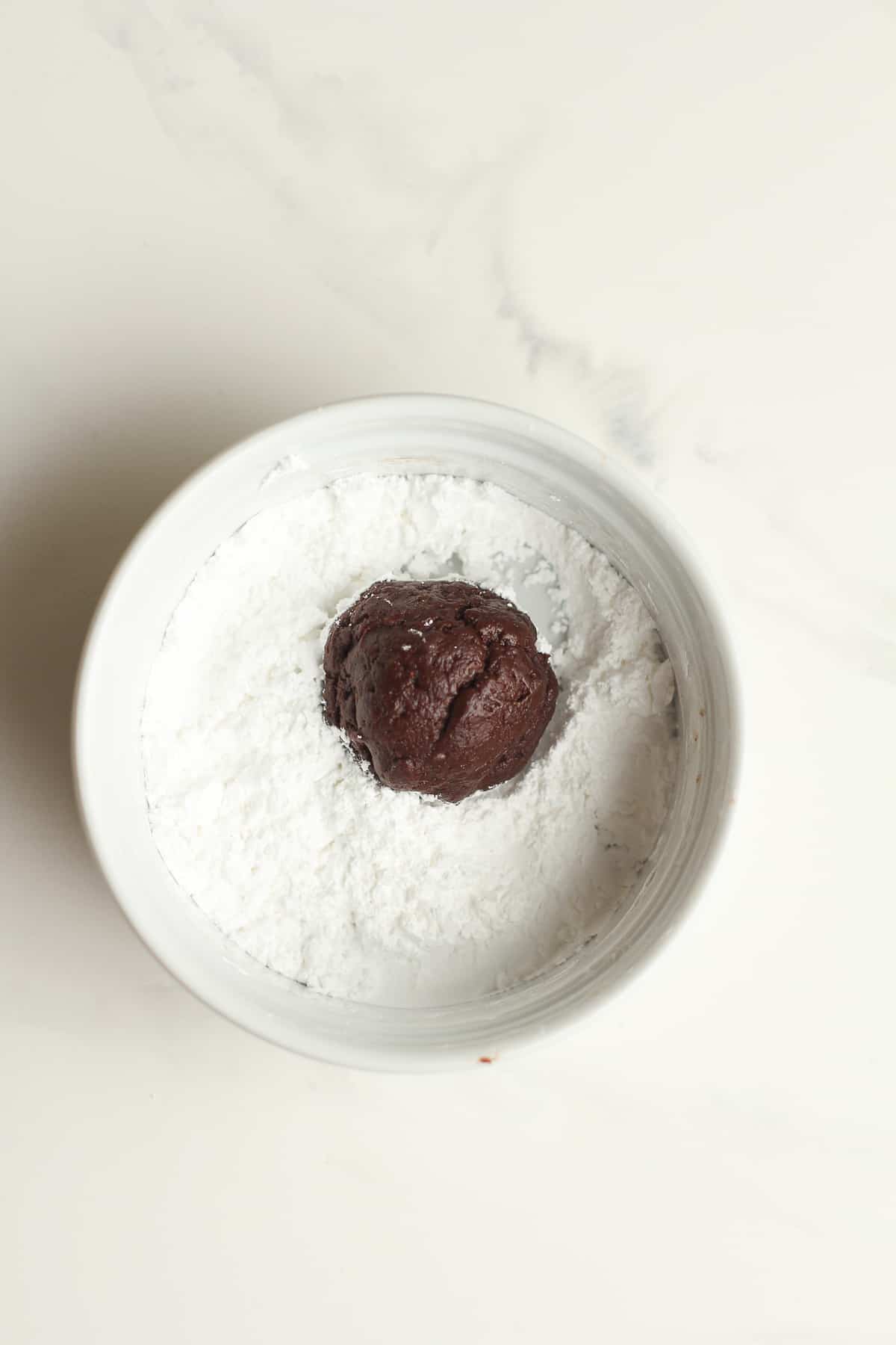 A bowl of the powdered sugar with a cookie ball.
