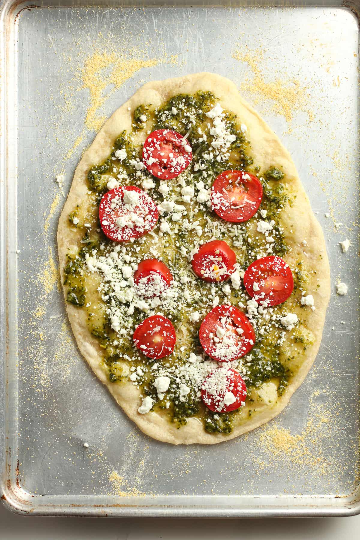 Pesto flatbread pizza on a pan before baking.