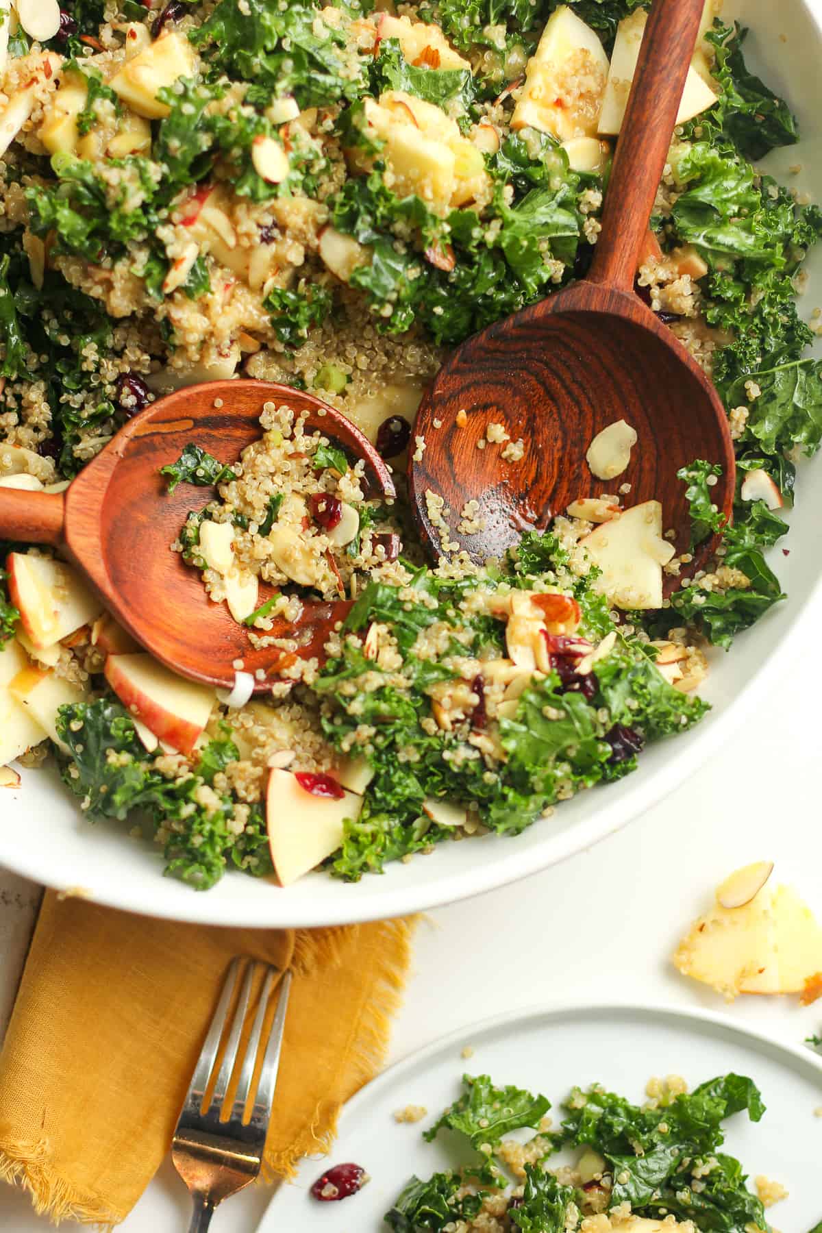 A partial bowl of kale and quinoa salad with wooden spoons.