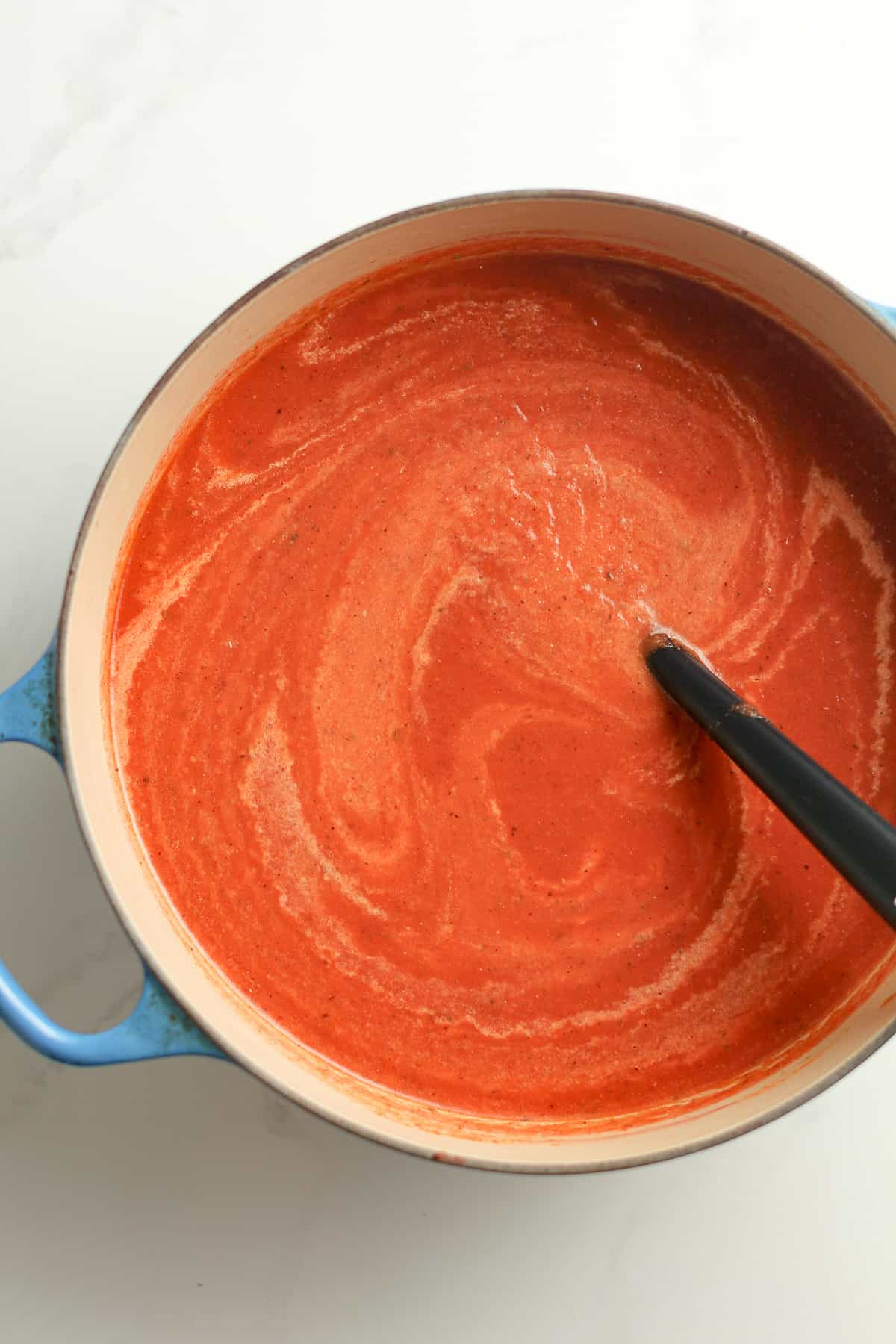 The pot of tomato soup with cream.