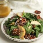 Side view of a serving of candied pecan salad, with a jar of dressing.