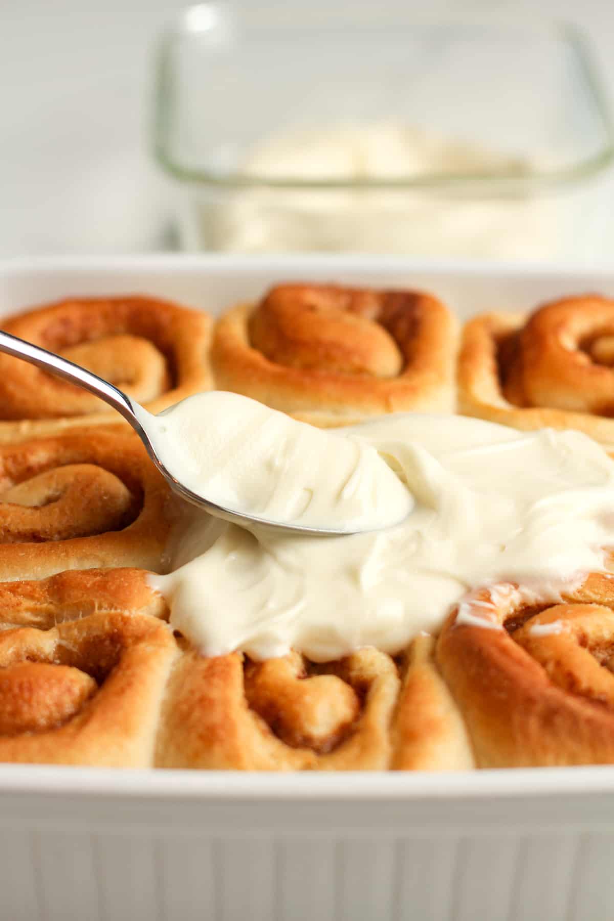Side shot of a spoonful of frosting on the baked rolls.
