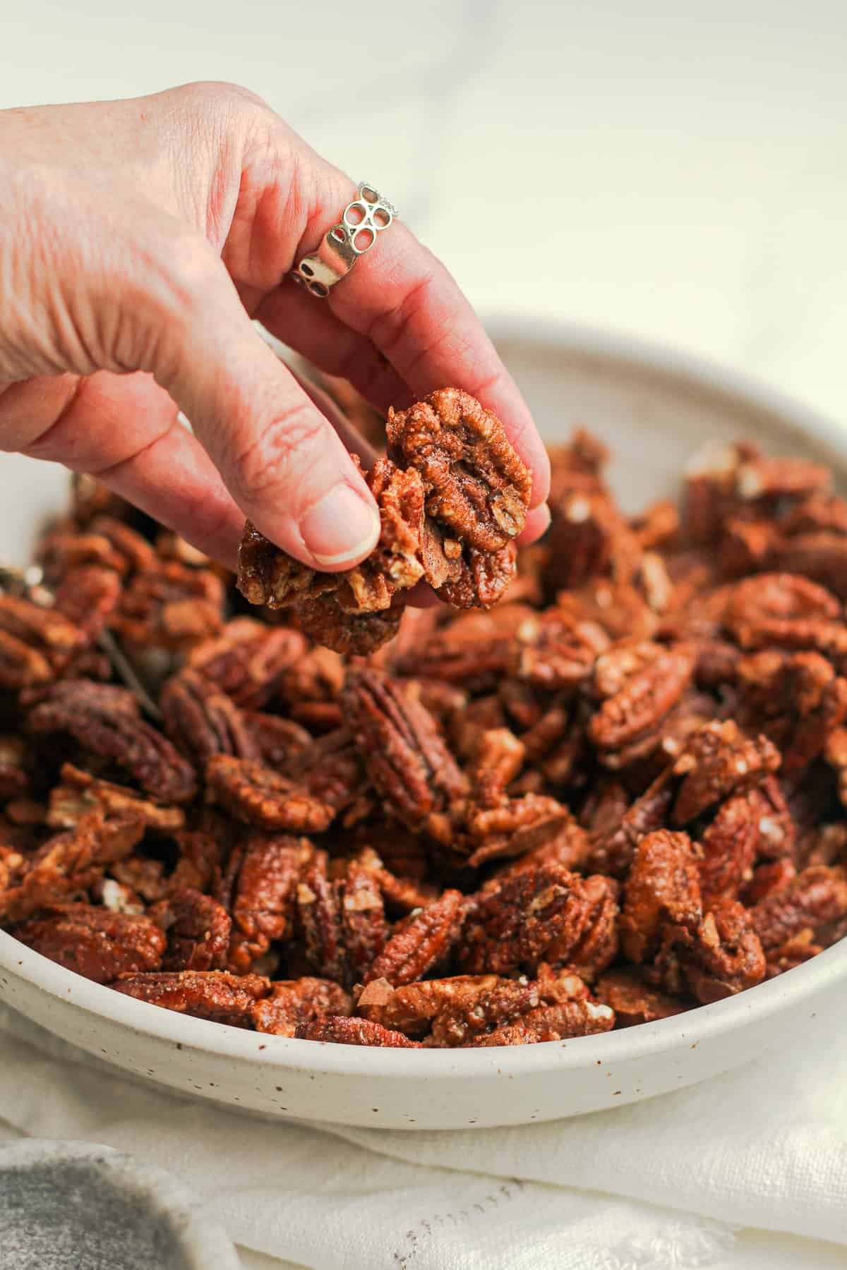 My hand holding some candied pecans over the bowl.