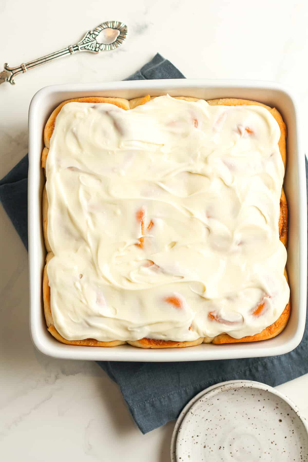 A square dish of baked homemade cinnamon rolls with cream cheese frosting on top.
