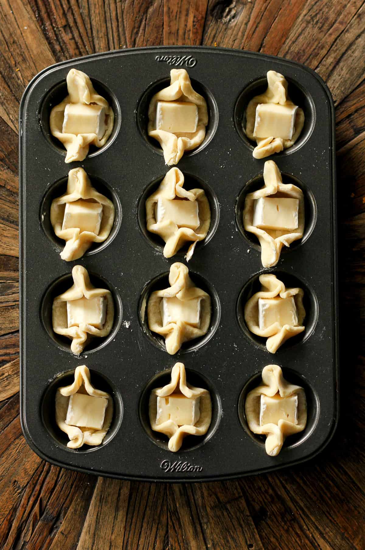 A muffin tin with the puff pastry and brie cheese.
