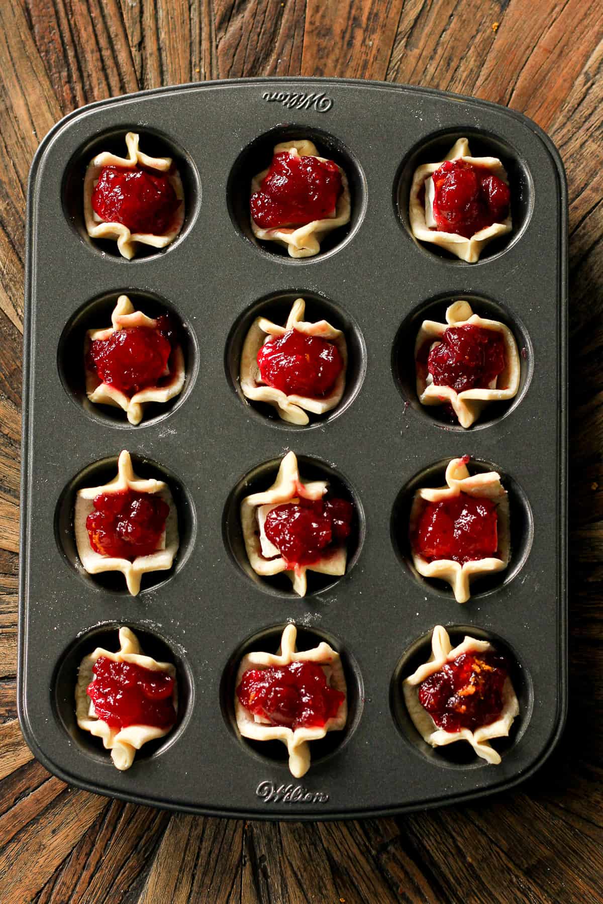 A muffin tin with puff pastry plus cranberries.