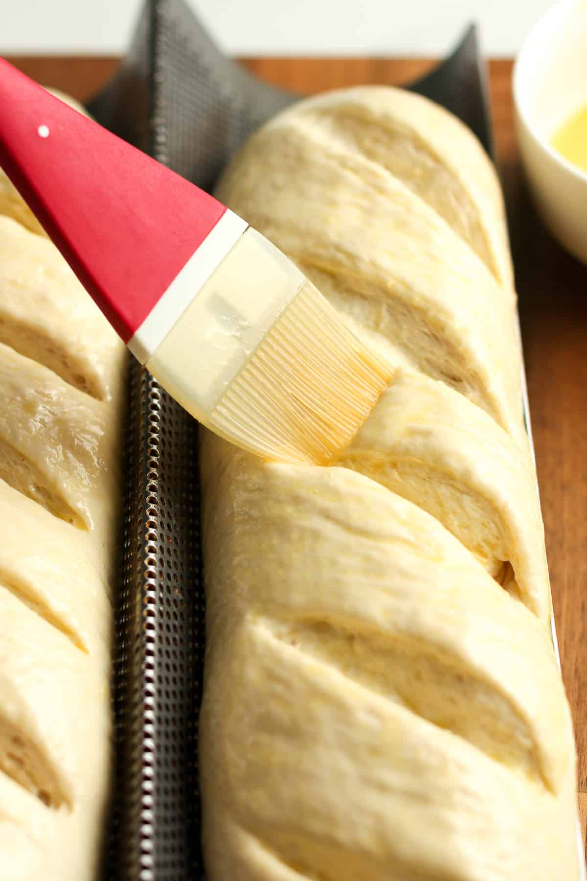 A brush on the loaves, spreading egg wash.