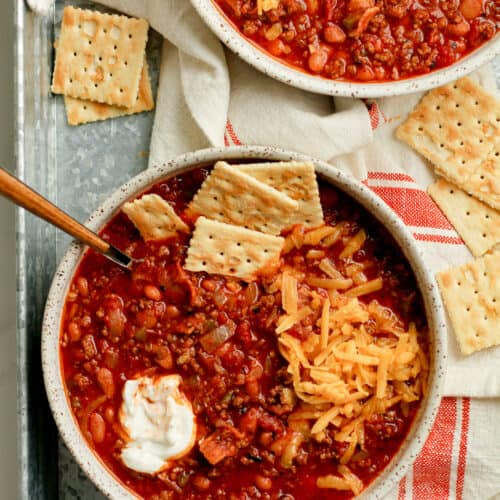 Two bowls of beef chilii with crackers.