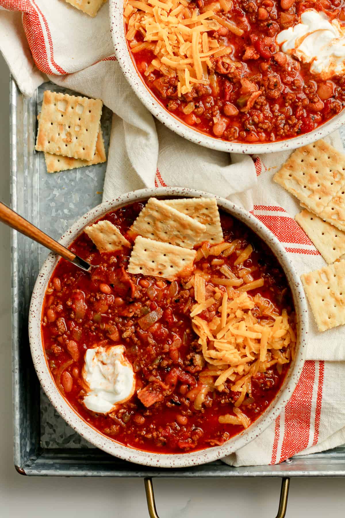 Two bowls of beef chilii with crackers.