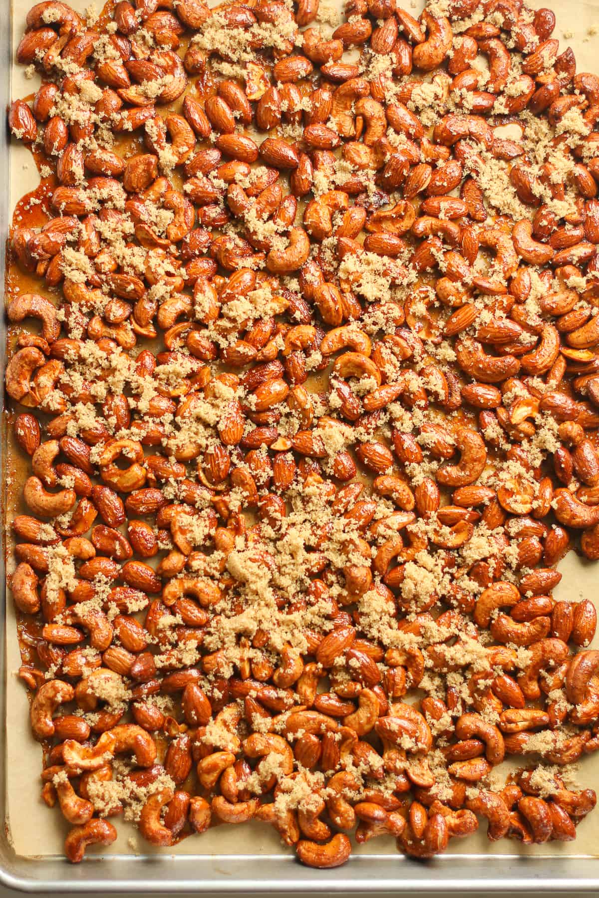 A sheet pan of the just roasted nuts with brown sugar sprinkled on top.