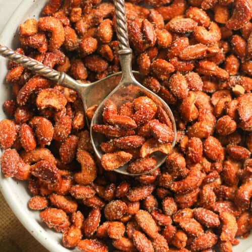 A bowl of the honey roasted nuts with serving spoons on top.