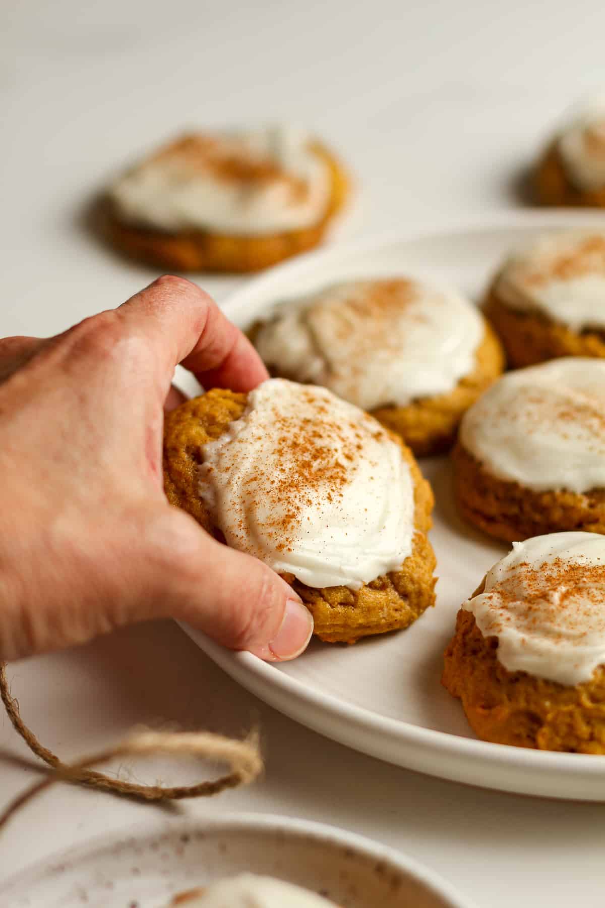 A hand picking up an iced pumpkin cookie from a plate.