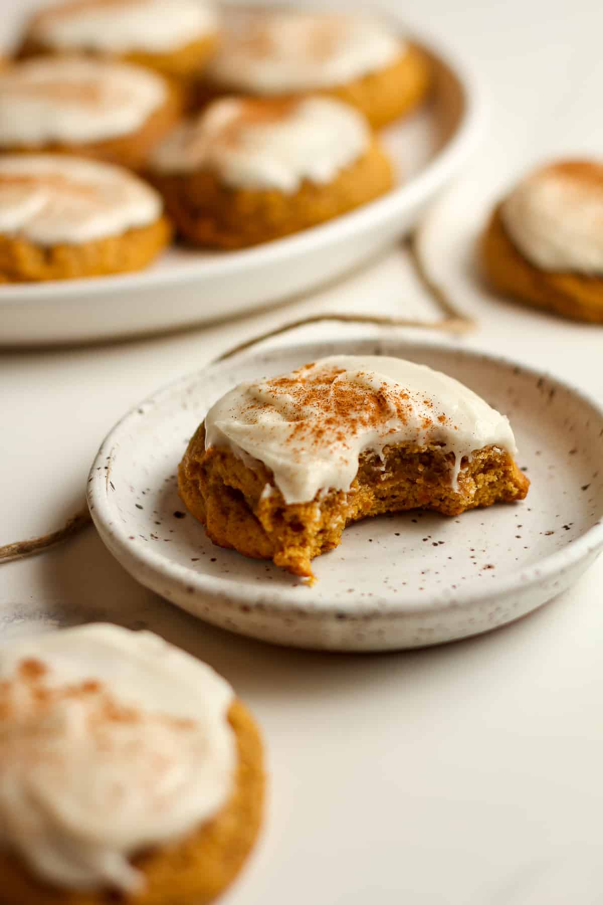 Side shot of a small plate of a pumpkin cookie with a bite out.
