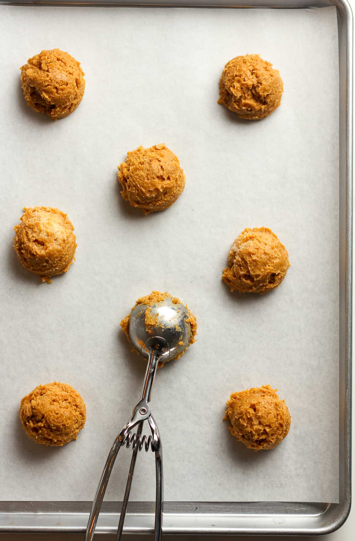 A pan with the pumpkin dough balls with cookie scoop.