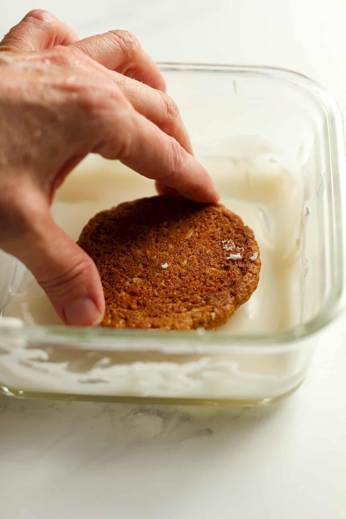 A hand dipping a cookie in icing.