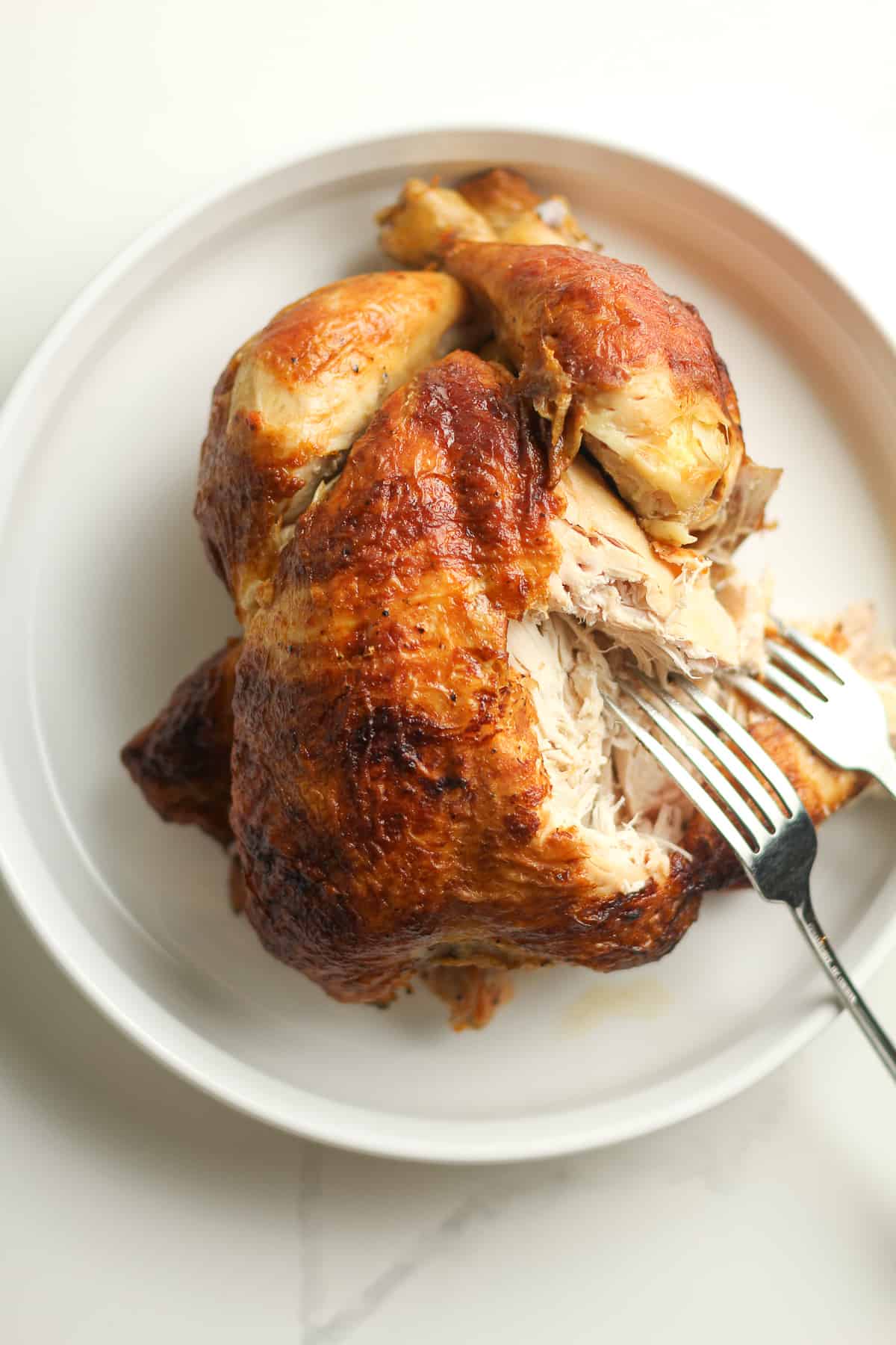 A plate of a rotisserie chicken with two forks.