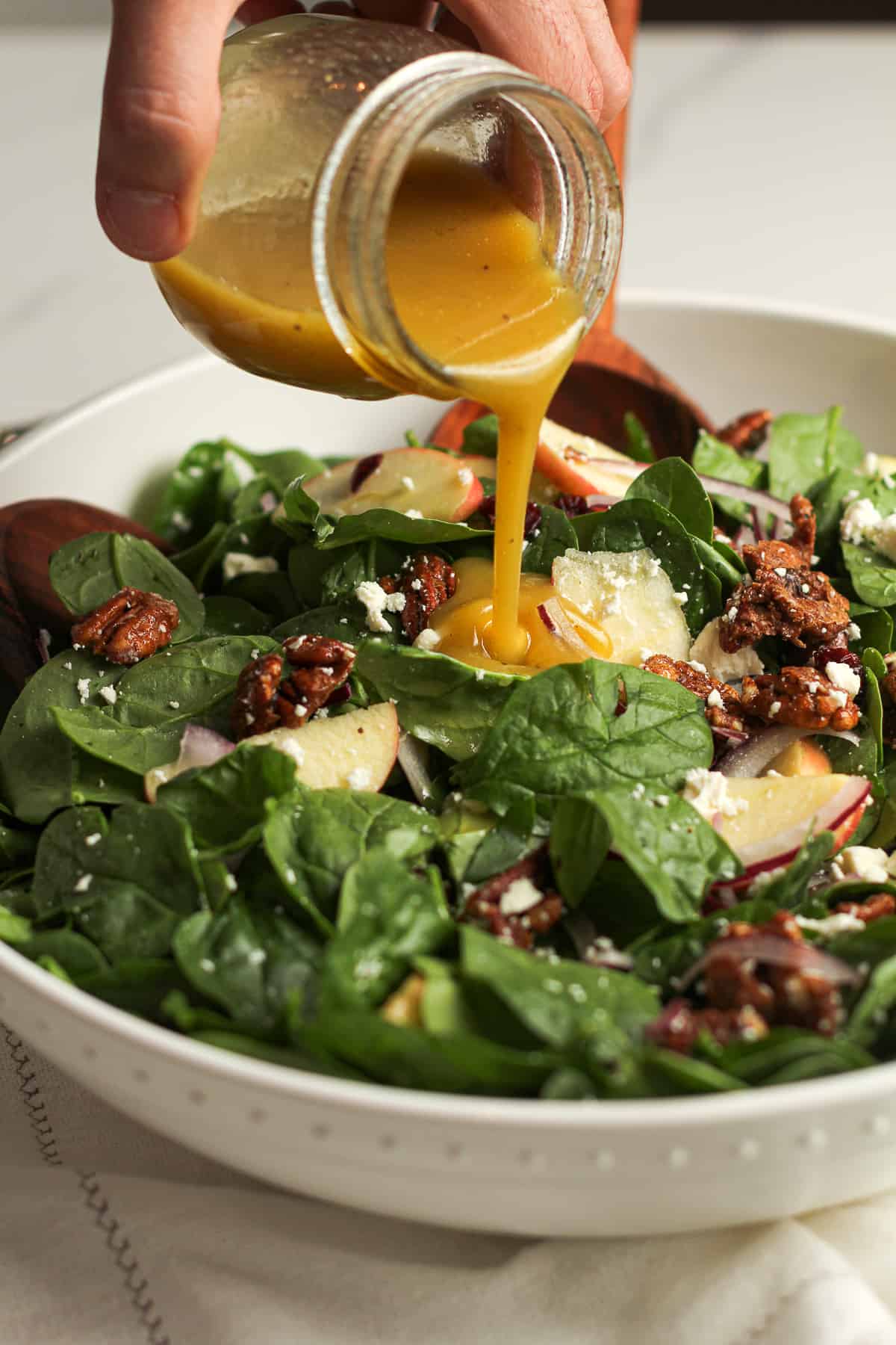A hand drizzling the dressing over the holiday apple salad.