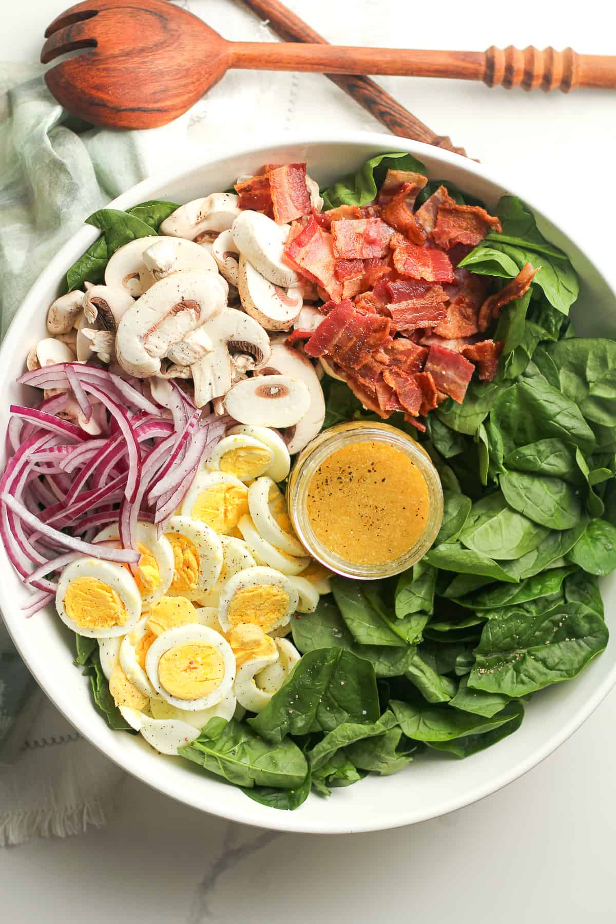 The bowl of spinach salad by ingredient with the jar of dressing.