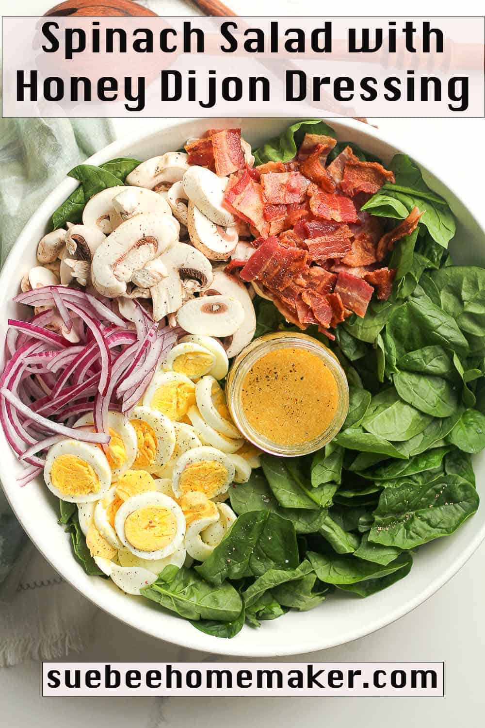 A large bowl of spinach salad by ingredient, with a jar of Honey Dijon Dressing.