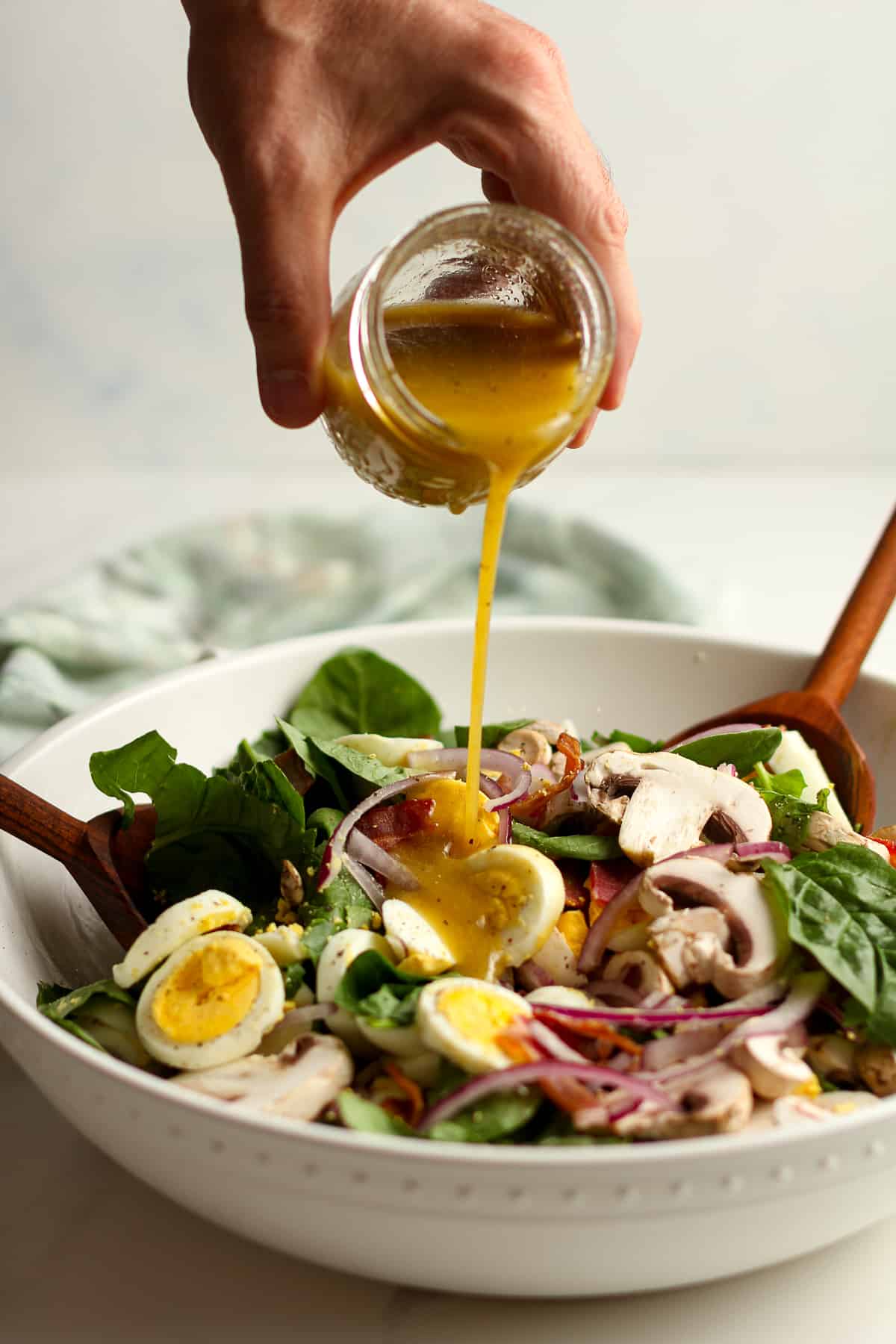 A hand drizzling a jar of Honey Dijon Dressing on the spinach salad.