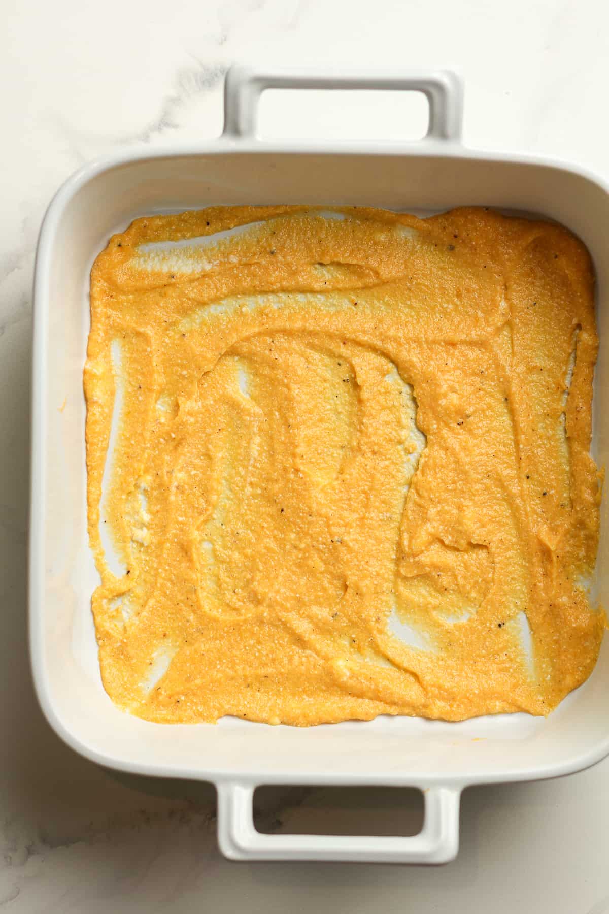 A square casserole dish with some squash puree on bottom of pan.