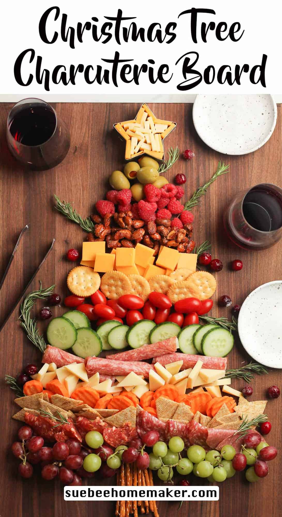 A board with a Christmas tree charcuterie board with small plates and glasses of wine.